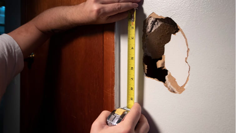 Manos de hombre midiendo un agujero para reparar la pared