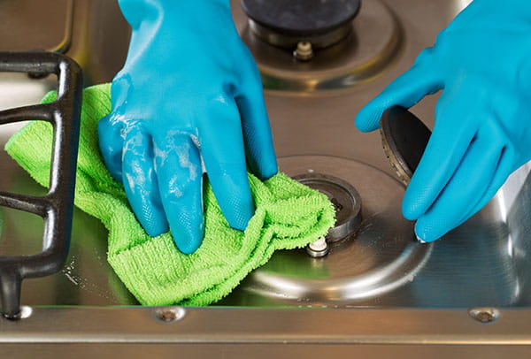 Manos con guantes limpiando los quemadores de una cocina de gas